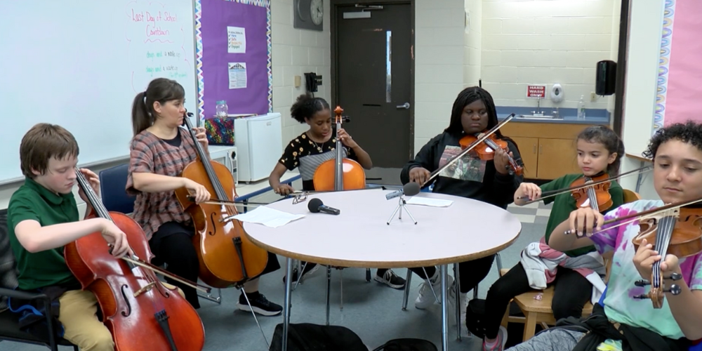 A group of students playing various kinds of string instruments with their teacher.