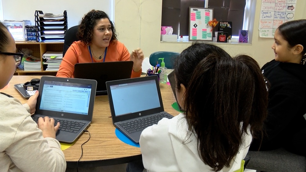 Teacher working with three students using laptop computers