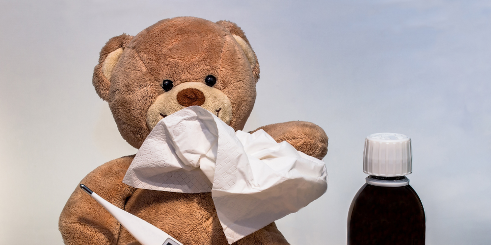 Teddy bear holding a tissue and thermometer, with a medicine bottle nearby