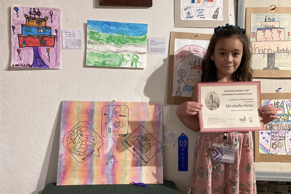 Student stands in front of art display while showing her award certificate 