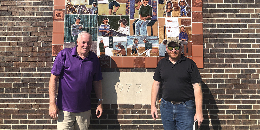 Two men standing in front of a mural made by students