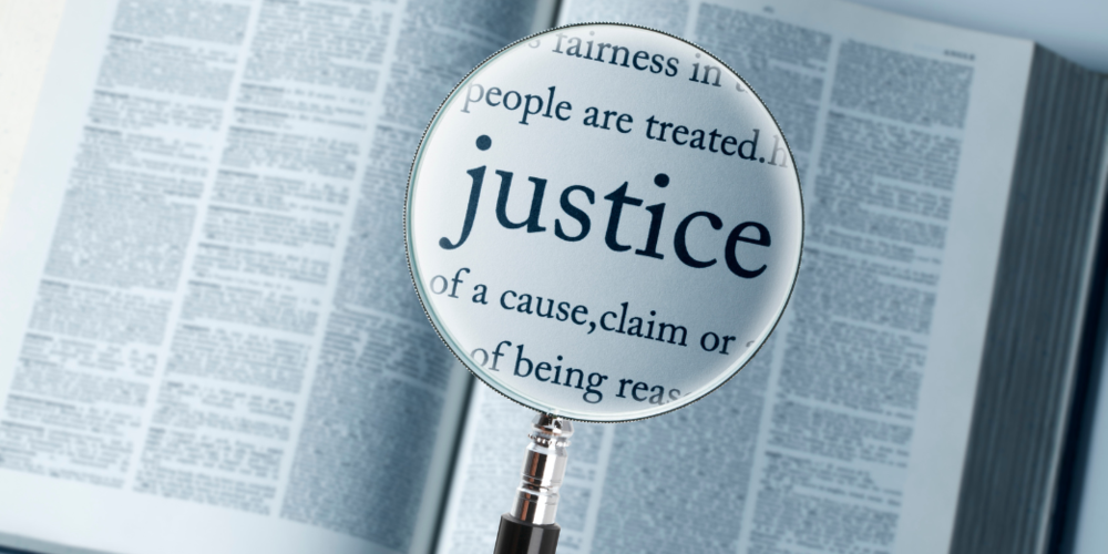 Magnifying glass highlighting the word Justice over an open dictionary