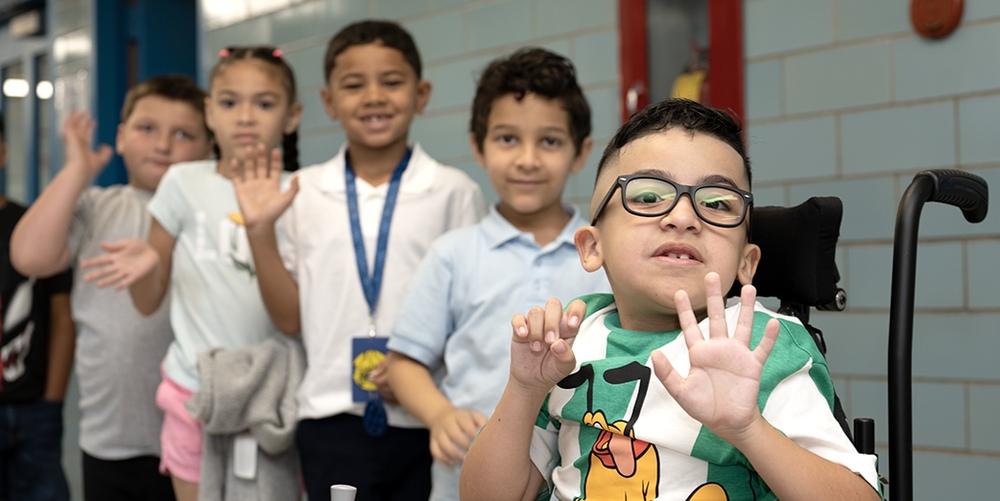 Five elementary students waving in hallway