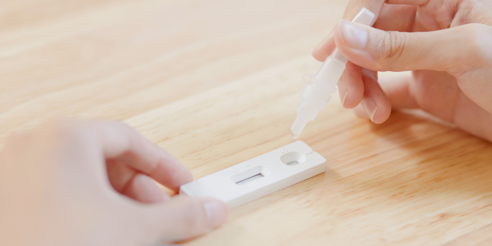 Two hands demonstrating how to drop solution into COVID-19 test kit