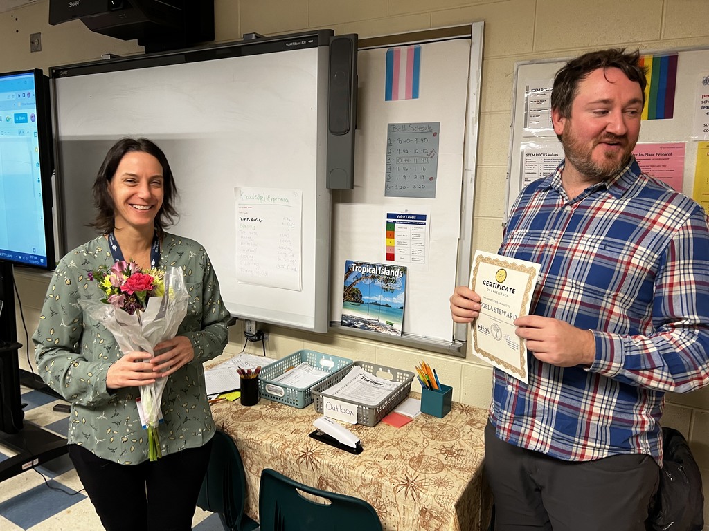 Two educators in classroom with certificate and flowers.