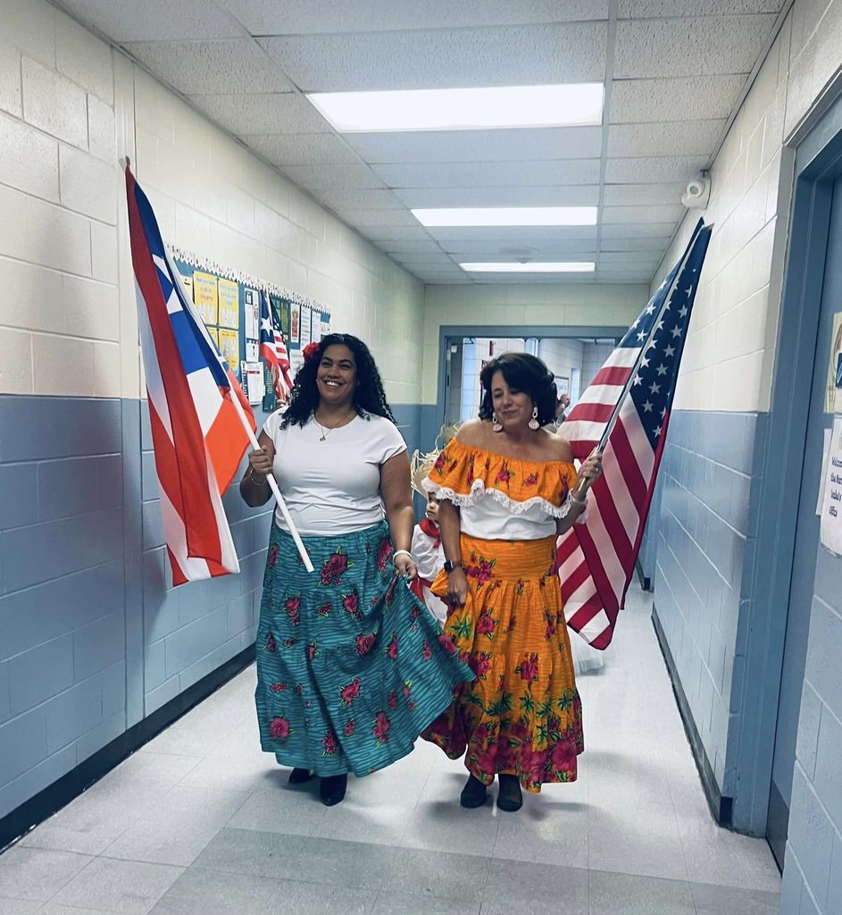 Picture of staff in traditional cultural dresses holding an american and puerto rican flag. 