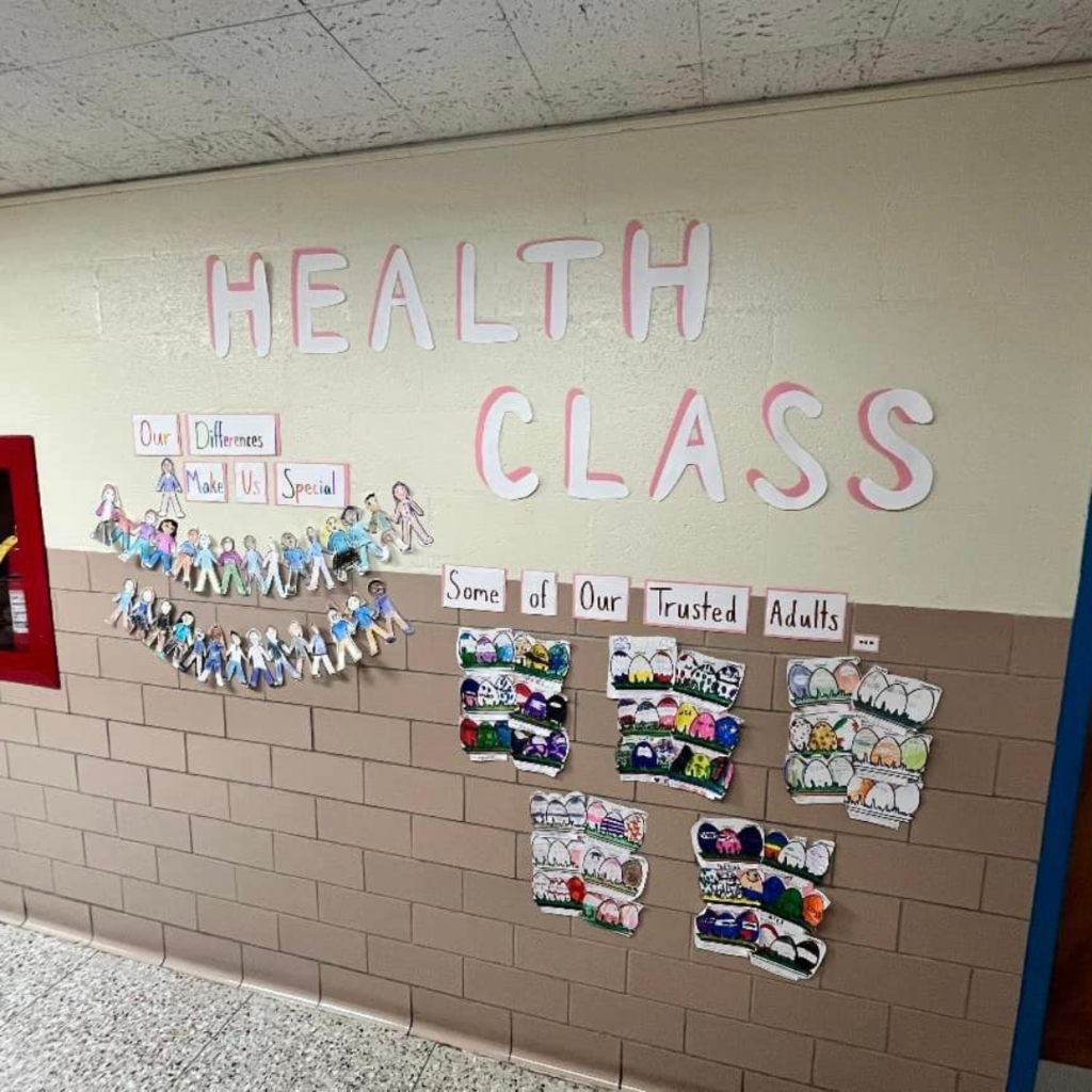 Cut-out paper letters on the wall that say "Health Class". Below is hung up paper dolls made by children.