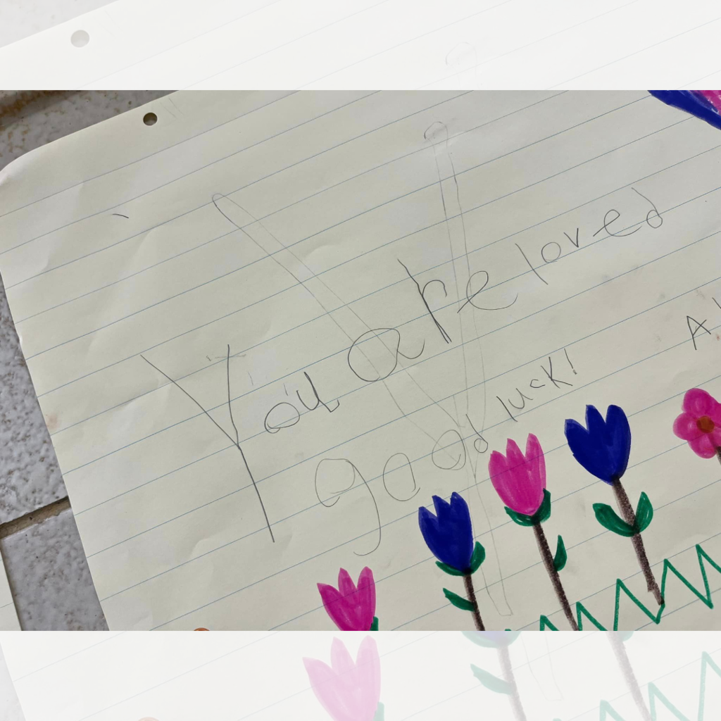 A poster with the words "You are loved. Good luck!" and a row of flowers drawn below.
