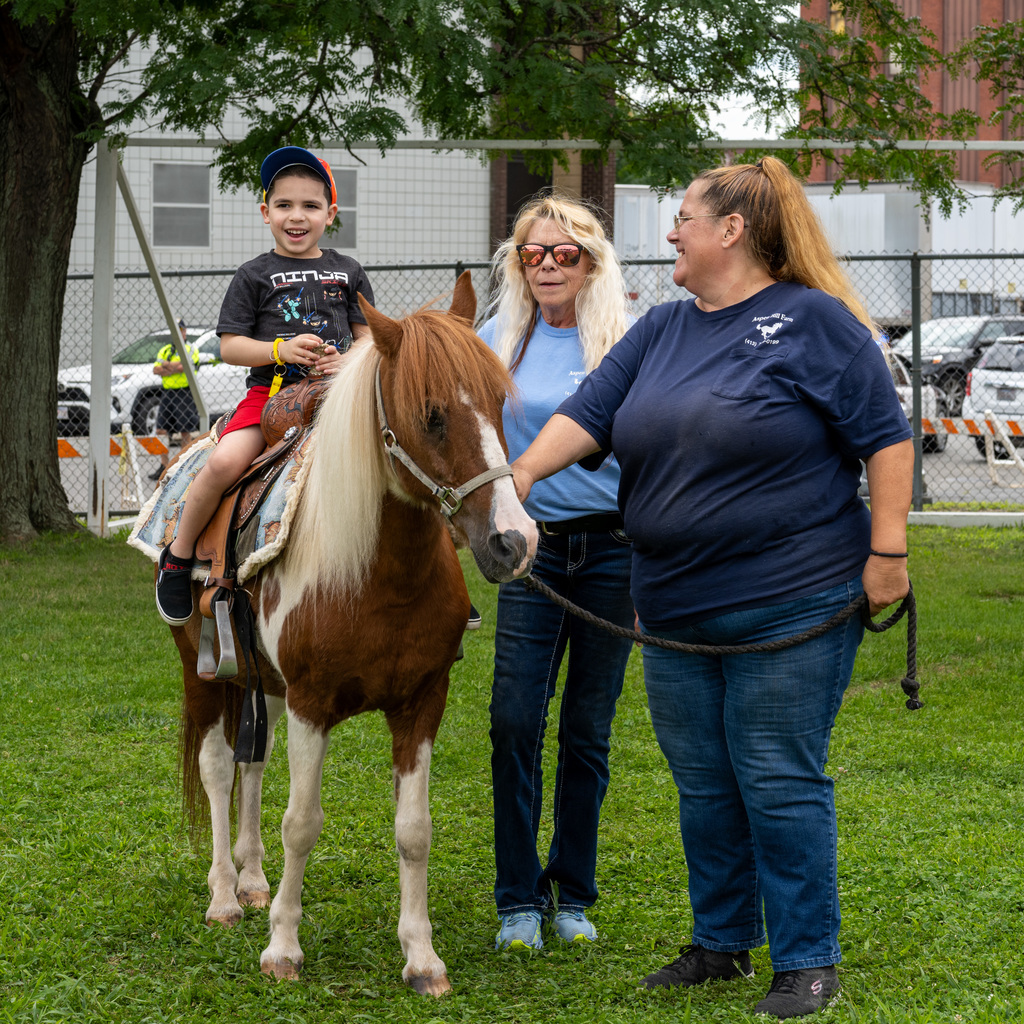 A young student riding a pony with the help of two trainers.